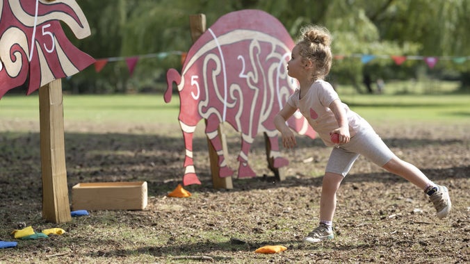 A little girl wearing pink clothes throwing a bean bag at an oversized cut out of an Anglo-Saxon animal